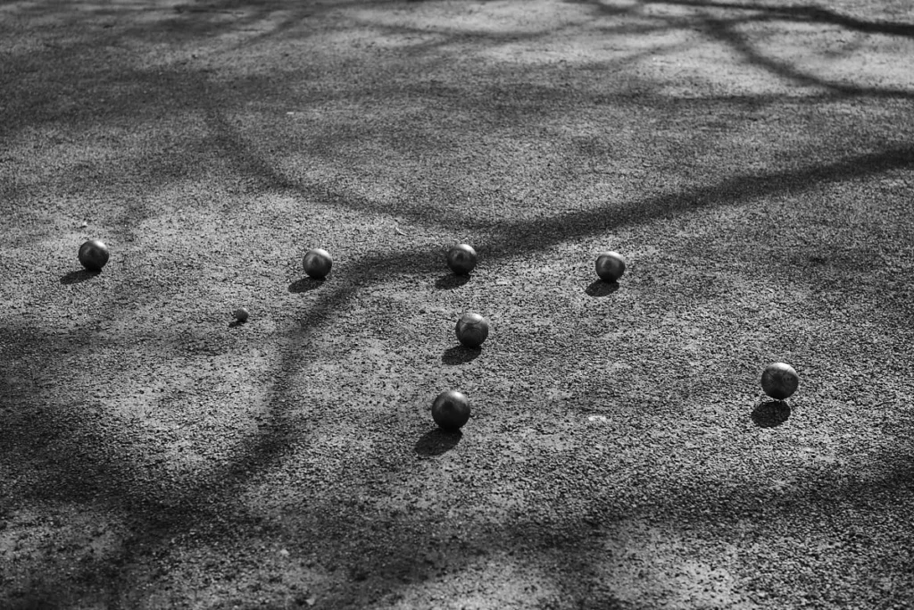 Asfalt zemin üzerinde siyah beyaz petank oyunu, topların keskin gölgeleri.