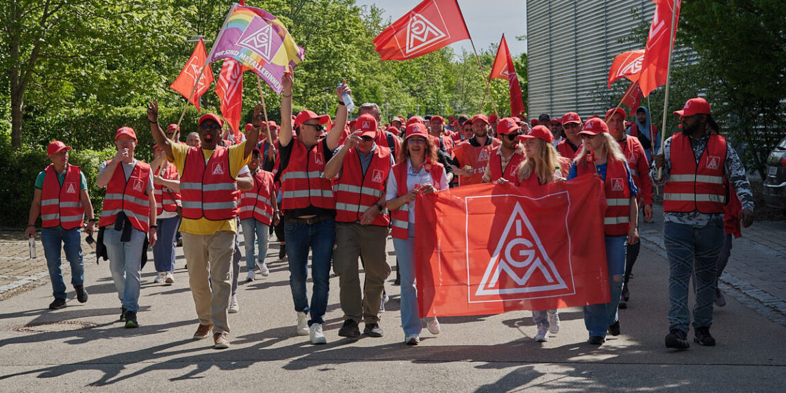 Begeisterte Avnet-Arbeiter in roten Streikwesten und mit Gewerkschaftsfahnen,