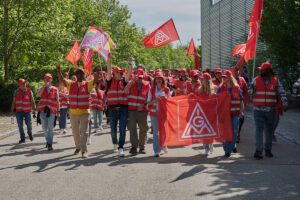 Begeisterte Avnet-Arbeiter in roten Streikwesten und mit Gewerkschaftsfahnen,